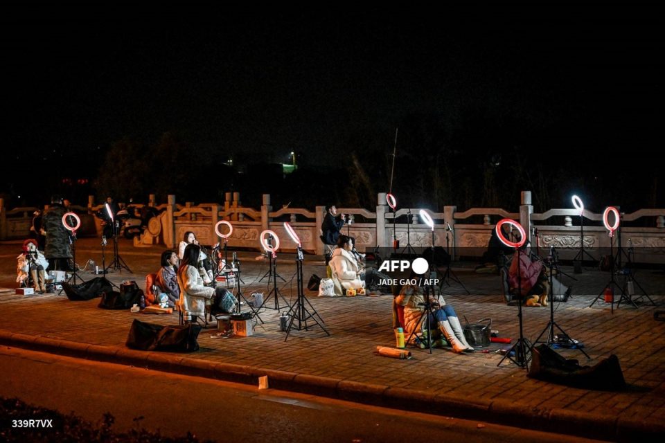 Jóvenes chinos se sientan frente a sus teléfonos inteligentes en un puente en medio de la noche para transmitir en vivo